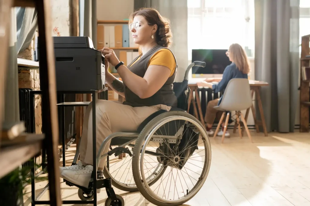 young-serious-disable-businesswoman-wheelchair-sitting-by-xerox-machine-pressing-start-button-while-making-copies-documents